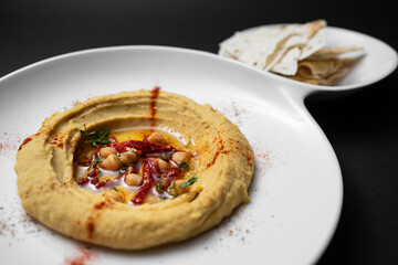hummus with chickpea, olive oil, paprika and pita bread on black background