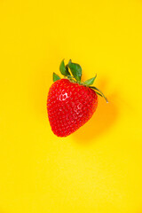 Close up of a red strawberry on a bright yellow background
