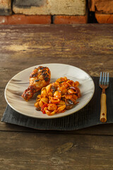 Seashell pasta in tomato and grilled chicken leg on a stand.