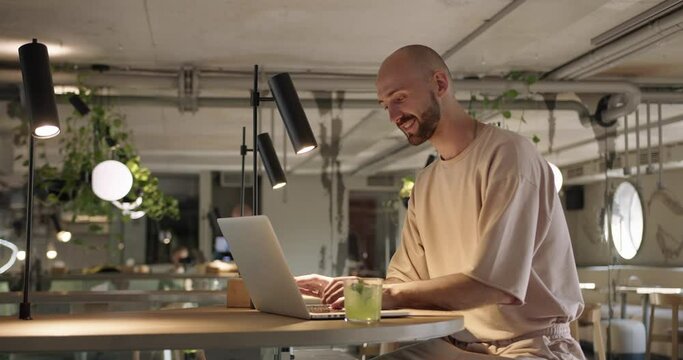Side view of smiling man typing on laptop at cafe