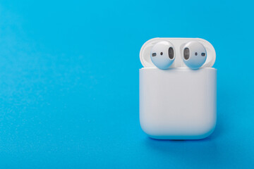 Modern wireless bluetooth headphones with charging case on a blue background. The concept of modern...