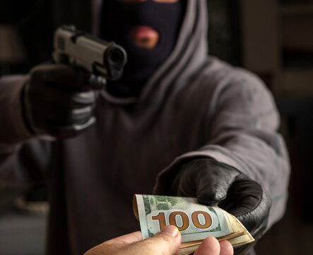Gloved hand holding a pistol stealing money, closeup view. Armed robbery concept