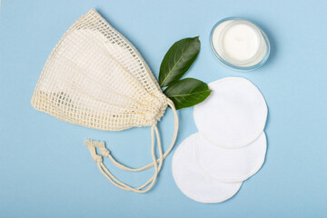 Cotton reusable make-up remover pads in a cloth bag and face wash and cleanser on a blue background. The concept of ecology and conscious consumption. Reusable cotton pads