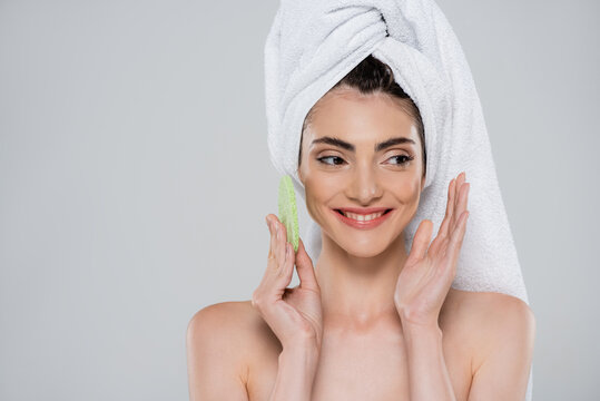 Cheerful Young Woman With Towel On Head Holding Green Beauty Sponge Isolated On Grey