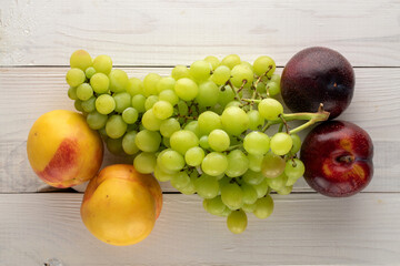 Two juicy ripe nectarines, a bunch of grapes and two plums on a wooden table, close-up, top view.