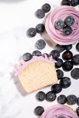 Homemade vanilla cupcakes with blueberry buttercream and fresh blueberries on top on a white marble background