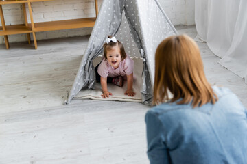 blurred kindergarten teacher looking at happy kid with down syndrome sitting in tipi © LIGHTFIELD STUDIOS