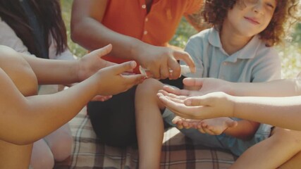 Close-up of young school teacher using sanitizing alcohol spray, disinfecting hands of multiethnic diverse elementary students outdoors. Infectious virus protection. Personal hygiene awareness - Powered by Adobe