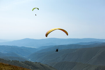Paragliding in mountains. Freedom to fly in air over mountains with parachute. Paragliding behind blue sky Carpathian Mountains hills range landscape. Active tourist sport People fly using Parachute.