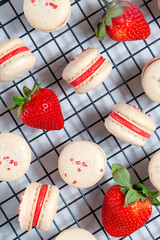 Homemade french macarons with strawberry buttercream and fresh strawberries on a cooling rack
