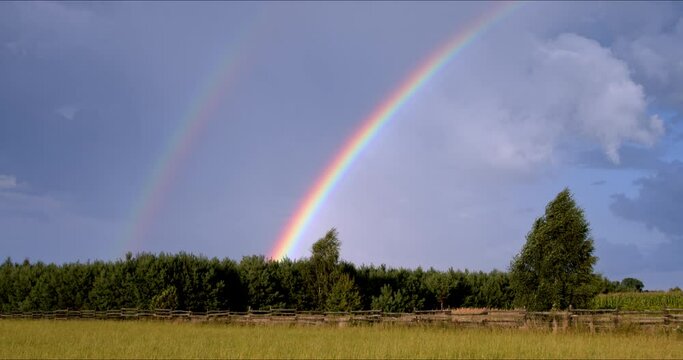 Double rainbow over grassland countryside landscape. Windy weather.