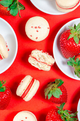 Homemade french macarons with strawberry buttercream and fresh strawberries on a bright red background