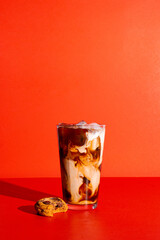 Tall glass of iced coffee with cream on a bright red background with a cookie