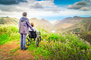 Young man and his wife in wheelchair travelling together in mountains