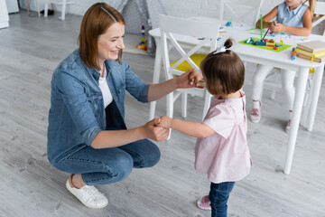 happy kindergarten teacher holding hands with disabled kid near preschooler girl