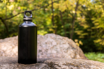 Black steel flask for water on a stone in the forest. The concept of a healthy lifestyle and care...