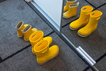 Close up view of yellow children's rubber boots on a mat near a cabinet with a mirror in hallway....
