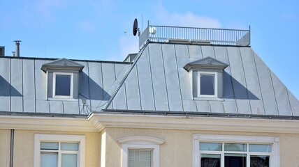 A gray metal roof in a stylish building. with wooden shutters and apartments in the attic with metal sheathed windows and roof chimneys 