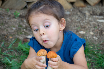 Little girl in a blue dress is holding orange-cap boletus mushrooms.