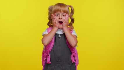 Oh my God, wow. Excited lovely little blonde teen child kid girl in school uniform raising hands in surprise looking at camera with big eyes, shocked by sudden victory. Back to school. Childhood