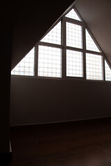 Loft, ático vacío con suelo de madera, paredes blancas y ventana triangular de vidrio. Lugar vacio sin personas. Ático donde realizar actividades. Fondo para fotomontajes.