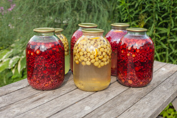 On the street on a wooden table there are jars with compote of red and yellow color