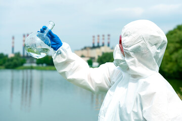 Sampling from open water. A scientist or biologist takes a water sample near an industrial plant. A...