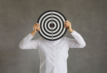 Woman hiding her face behind a shooting target standing on a grey studio background. Concept of...