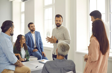 Small group of diverse women and men listen to a confident male corporate business coach. Man...