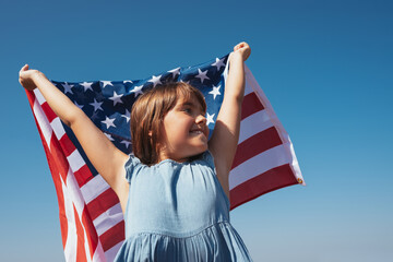 Portrait of a happy girl with the American flag in her hands against the background of the sky © Andrii