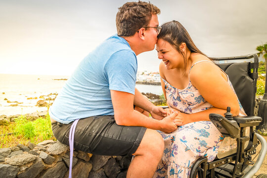 Disabled woman in wheelchair holding hand of her boyfriend while dating outdoors