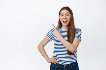 Obraz premium Image of happy young woman pointing at upper left corner, store product and smiling, showing announcement, sale info, standing over white background