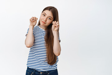 Cute young woman showing kawaii paws gesture and making coy face expression, standing against white background