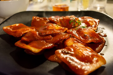 Traditional Italian ravioli filled with ricotta cheese, served with tomato sauce and basil leaves on a black plate. Close up.