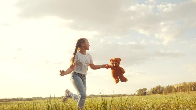 little girl with a teddy bear run in the park on the grass. happy family kid dream concept. little girl run in the park holding a teddy fun bear. happy childhood dream. kid walk in the park