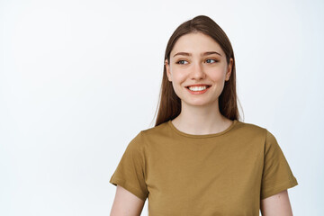 Fototapeta premium Image of young hopeful woman smiling happy, looking aside at empty space for banner, sale advertisement, standing over white background