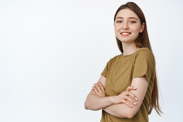 Obraz premium Young professionals. Smiling girl cross arms on chest and looking confident at camera, standing in tshirt against white background