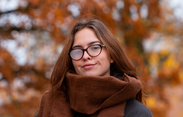 cute happy girl wearing a scarf in autumn in the park in glasses for vision - obrazy, fototapety, plakaty
