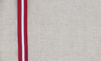 Composition of national latvian patterned ribbon flag on linen fabric - obrazy, fototapety, plakaty
