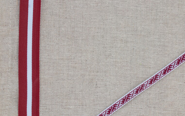 Composition of national latvian patterned ribbon and flag on linen fabric - obrazy, fototapety, plakaty