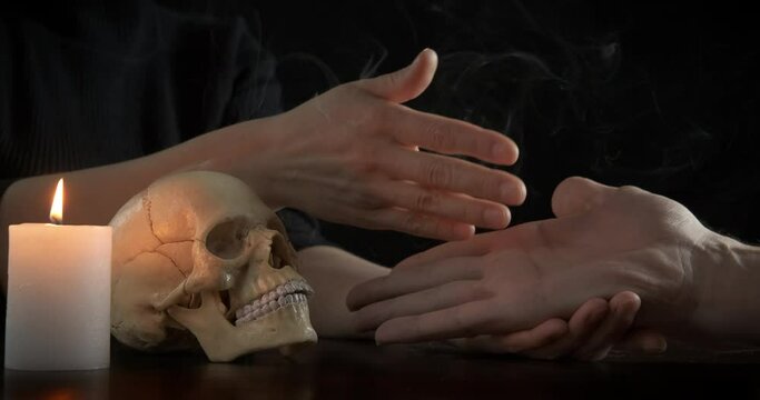 Woman read the hand future. A woman read the future on man's hand by the human skull and candle in the dark room. A concept of making magic and rituals at home.