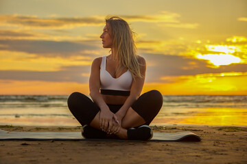 Fototapeta na wymiar Yoga during sunset on shore by woman on mat.