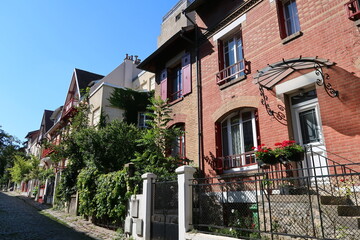 Fototapeta na wymiar Façade colorée d'une maison en brique rouge du square de Montsouris, ruelle pavée pittoresque à Paris (France)
