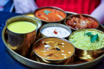 An Indian thali meaning steel plate containing different food items on a round platter such as Basmati rice, curd or Raita, Butter chicken and Mango lassi etc i