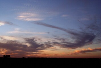 Atardecer en el campo con pinceladas de acuarela en el cielo azul con nubes gris plomo y blancas,...