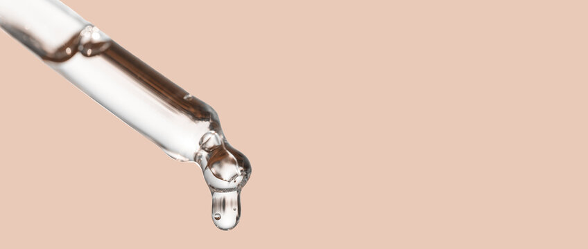 Cosmetics dropper, falling drop close up. Closeup of cosmetic pipette with essential oil dropping, serum with peptides on beige background. Self care concept. Beauty skin care product. Banner
