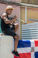 Latino man playing a trumpet sitting on a wall with the Dominican Republic flag: Selective focus. © JeanPaul