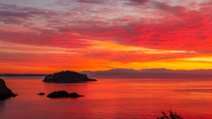 A vibrant red yellow orange sunset over the ocean waters with the Cascade Mountains in the distance...