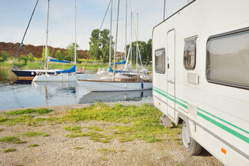 White caravan trailer and a car parked in a yacht club (marina), sailboats in the background....