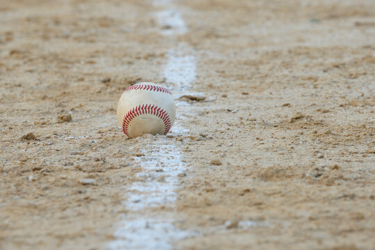 Long telephoto image of a well worn baseball sitting on the foul line leading to first base